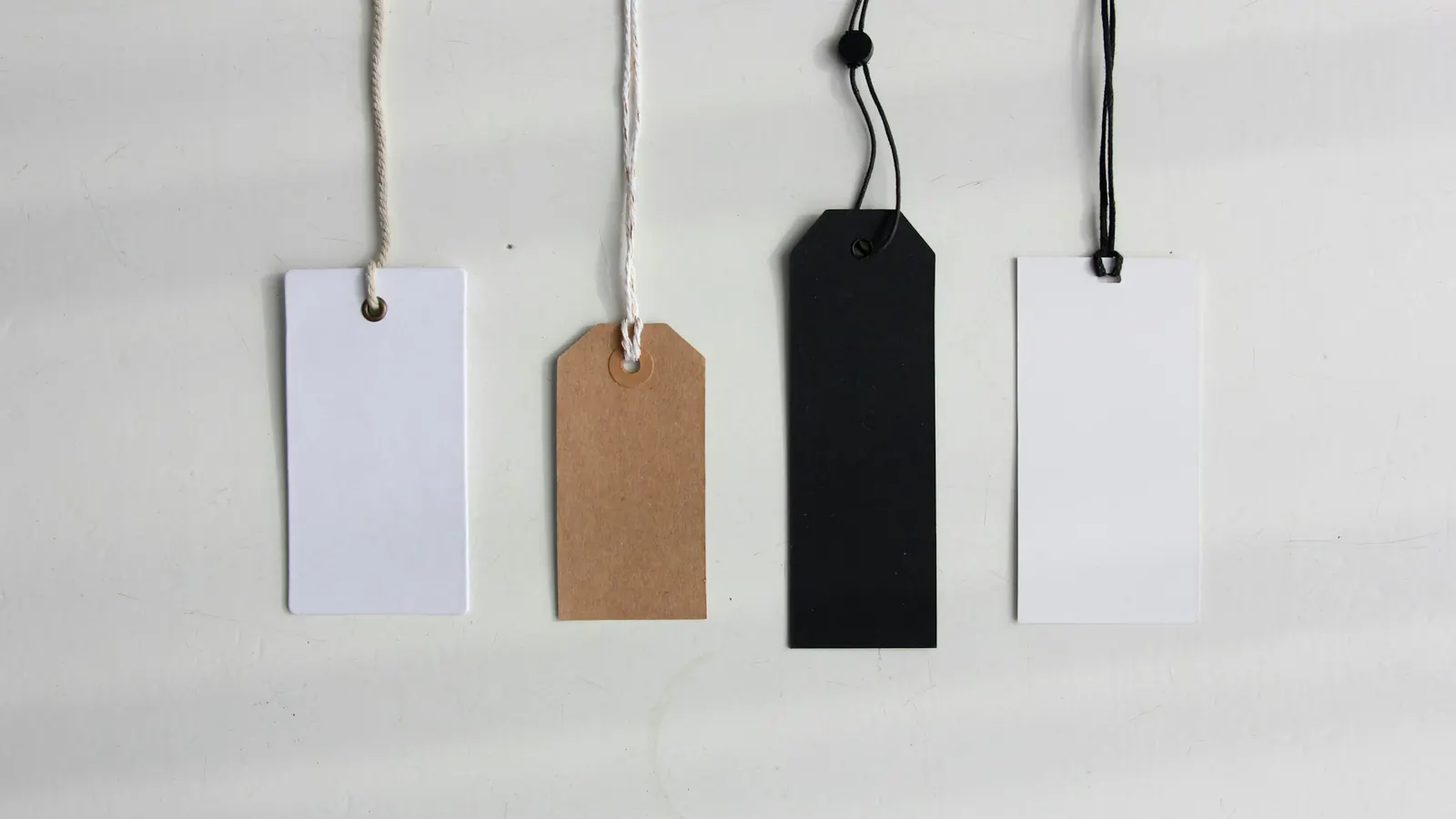 Four blank price tags hanging on a pale wall