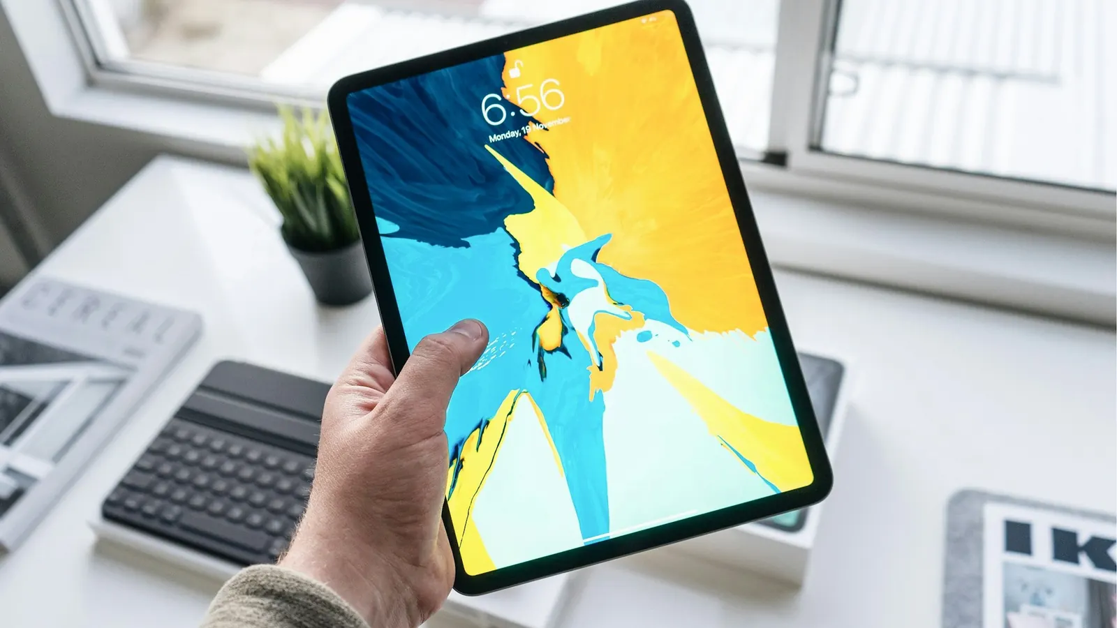 A hand holding an iPad over a white desk
